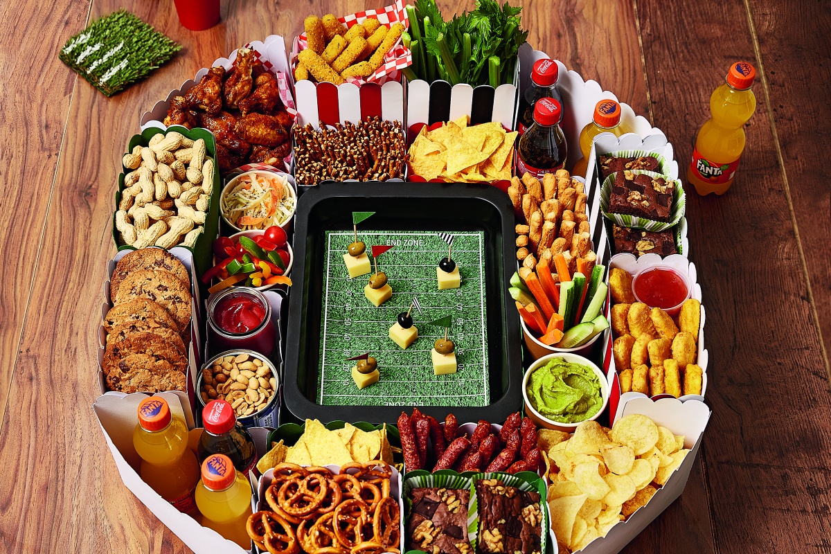 Aus bunter Pappe gebasteltes Snack-Stadion im American-Football-Design mit Chips, Gemüse, Dips, Brownies, Getränken und Fingerfood.