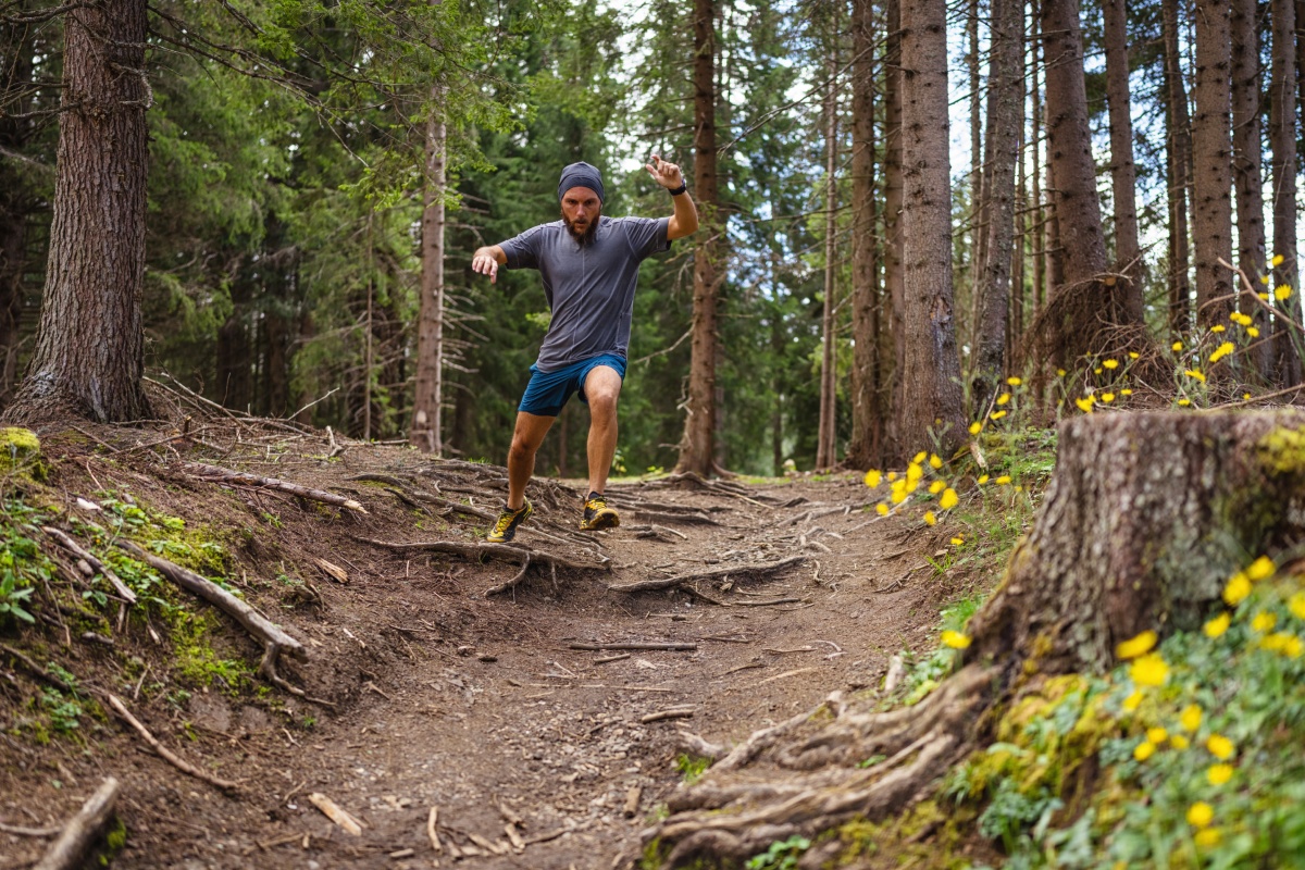 Mann joggt im Wald einen wurzeligen Hang entlang im Wald.