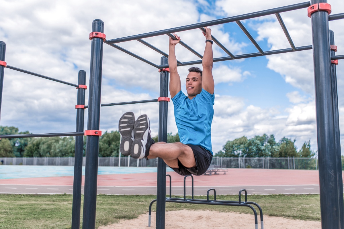 Mann in Sportkleidung macht Leg-Raises an einer Sprossenwand auf einem Sportplatz.