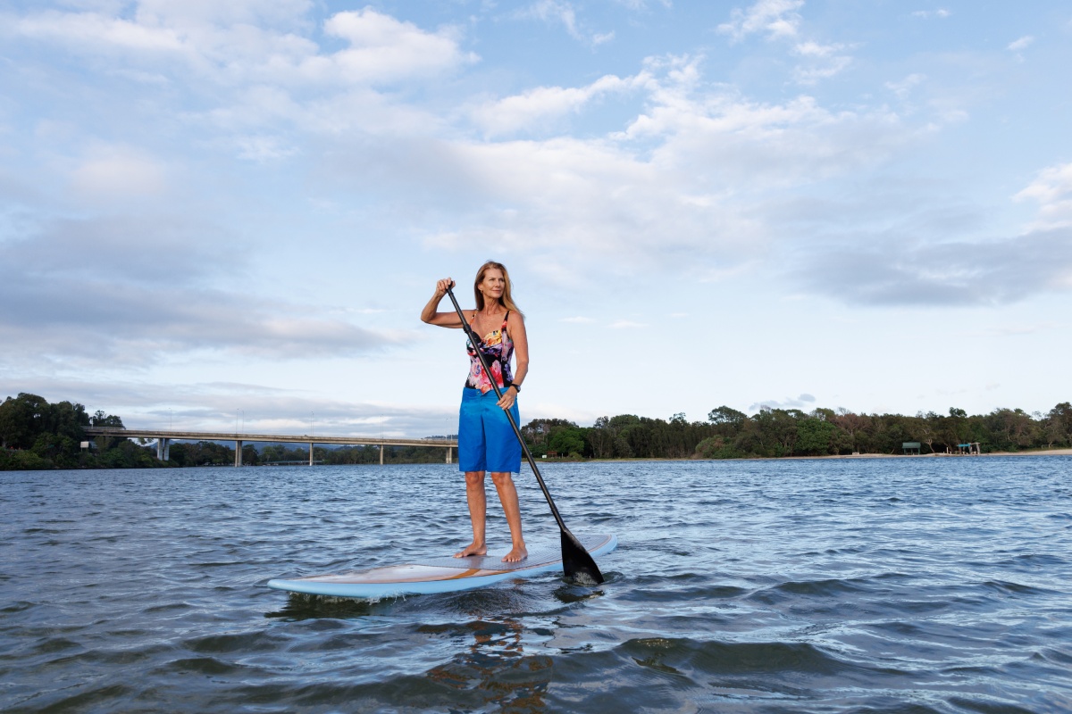 Frau in Badeanzug und Shorts macht Stand-Up-Paddling auf einem See
