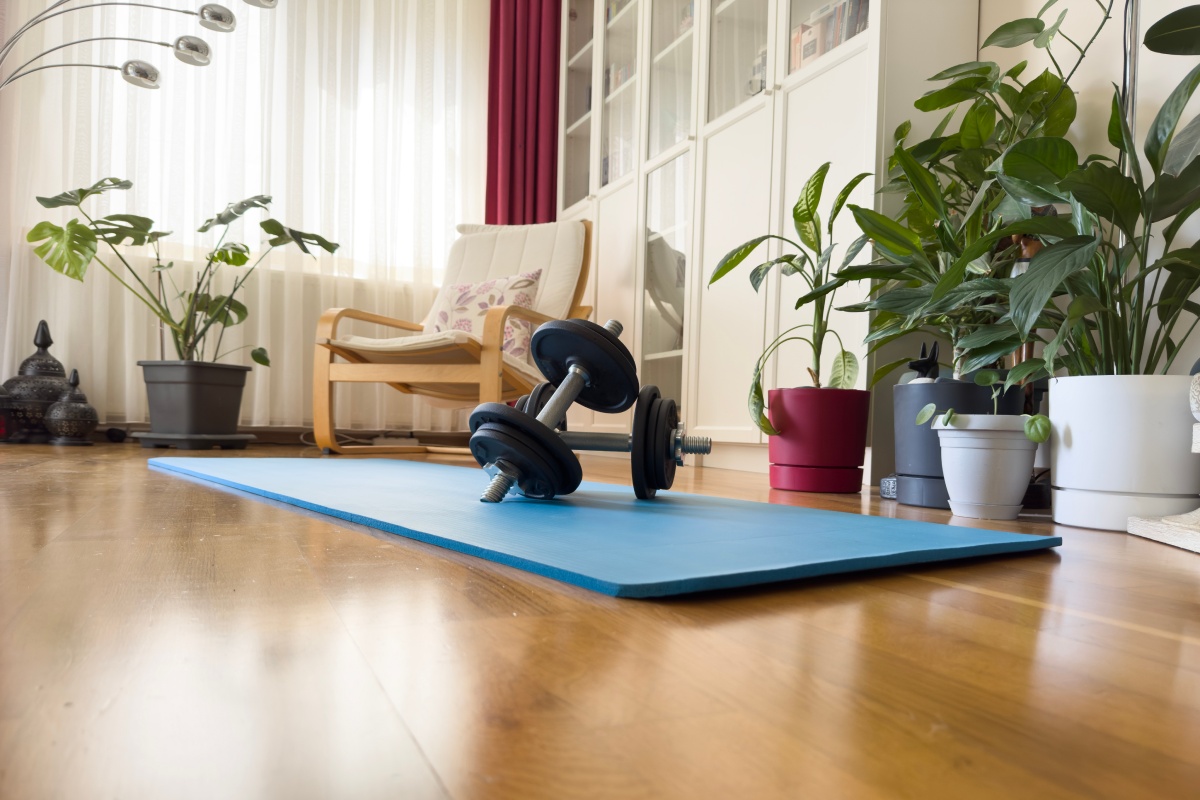 Hanteln liegen auf blauer Yogamatte in gemütlichem Wohnzimmer mit Holzboden.