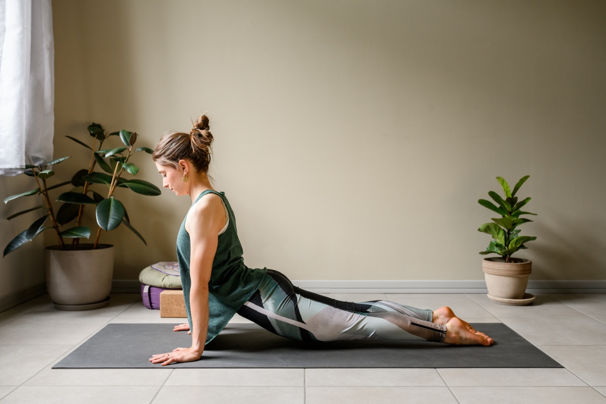 Frau macht Yoga-Kobra-Position auf grauer Matte in schlichtem Raum.
