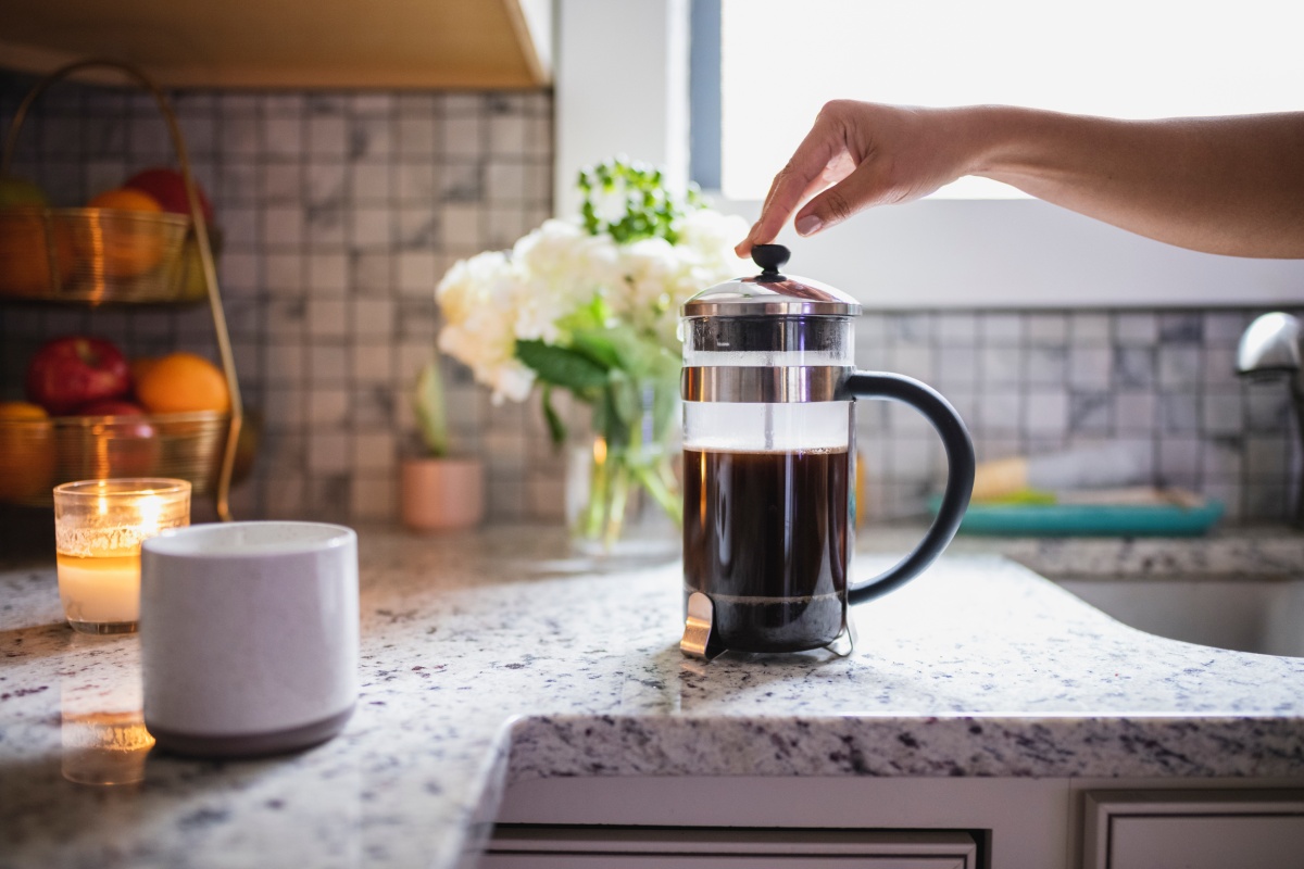 Eine Person drückt zum Kaffee kochen den Kolben einer French Press auf der Küchenarbeitsplatte.