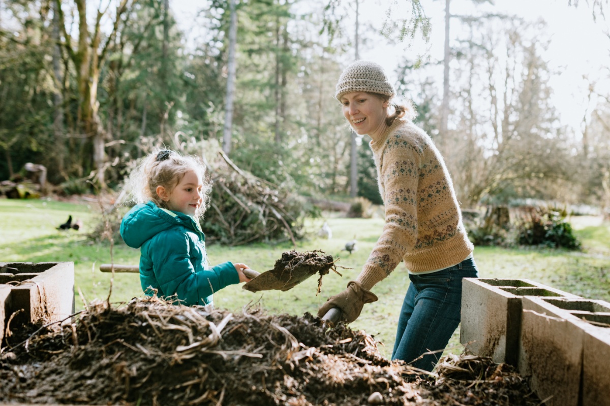 Frau und Kind im Grünen ernten mit Schaufeln Kompostgut.