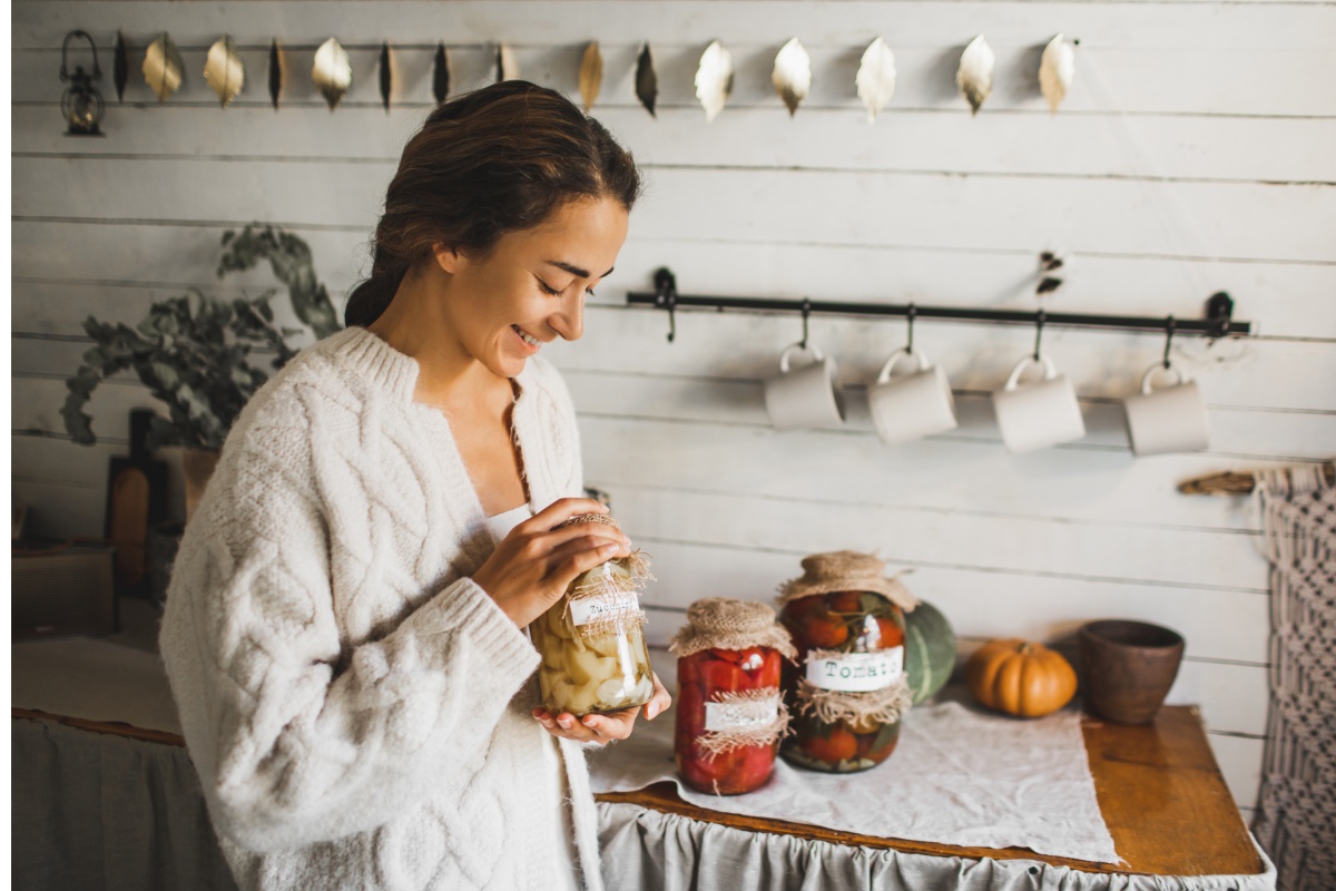 Eine junge Frau mit drei Gläsern eingelegter Lebensmittel.