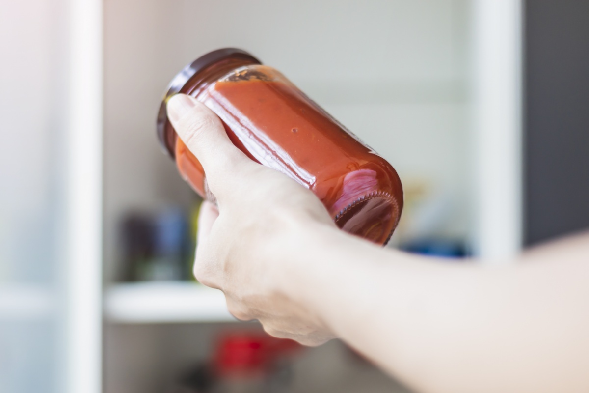 Eine Hand hält Tomatensoßen im Vorratsglas.