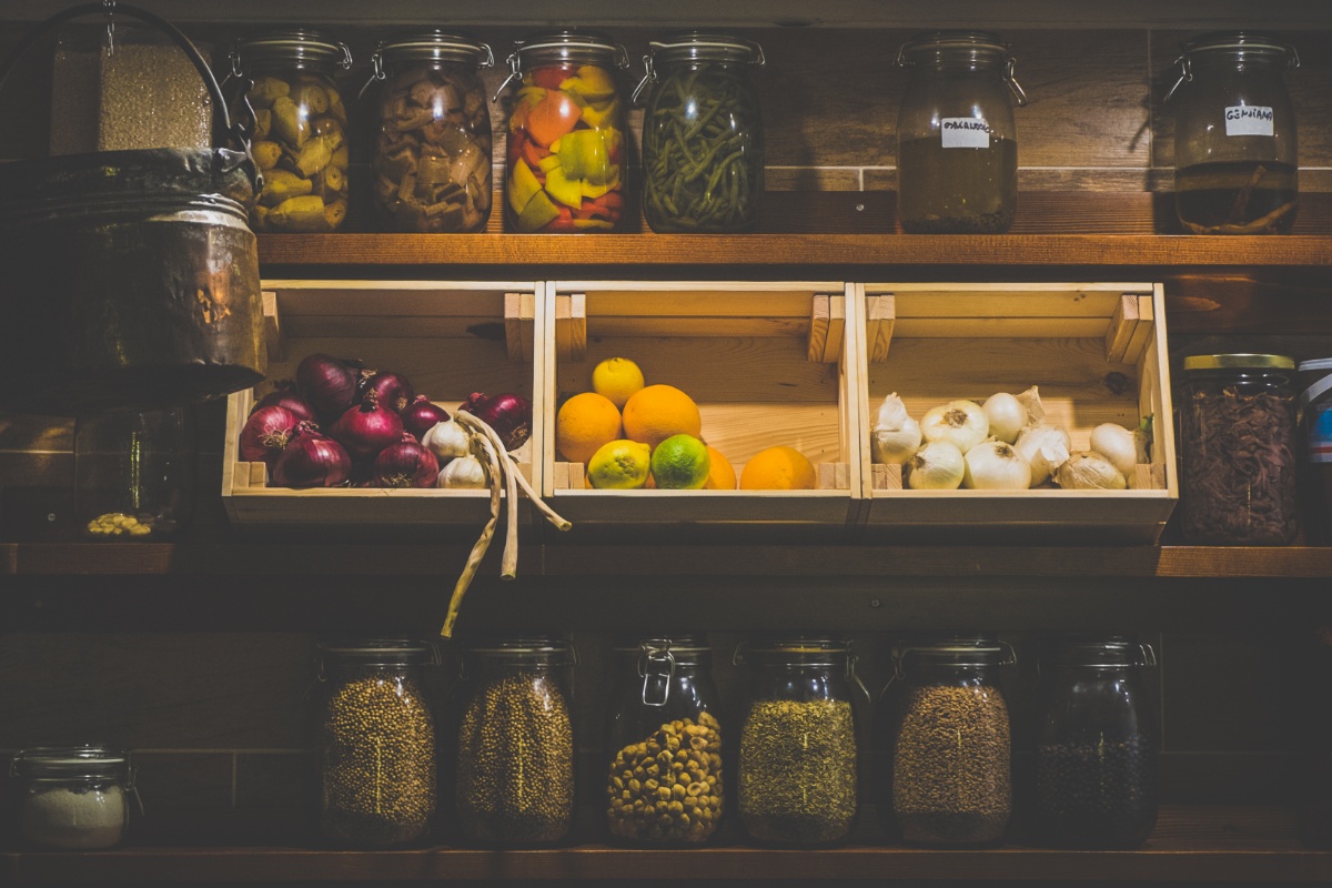 Dunkle Vorratskammer und drei hell erleuchtete Holzkisten mit Zwiebeln, Knoblauch und Zitronen, Orangen und Limetten.