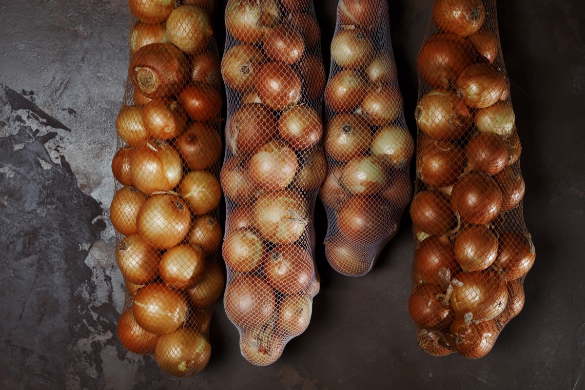 Zwiebeln im Vorratsnetz hängen in einem dunklen Raum.