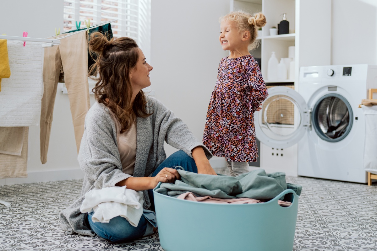 Eine Frau und ein Mädchen stehen an einem Korb voll Buntwäsche.