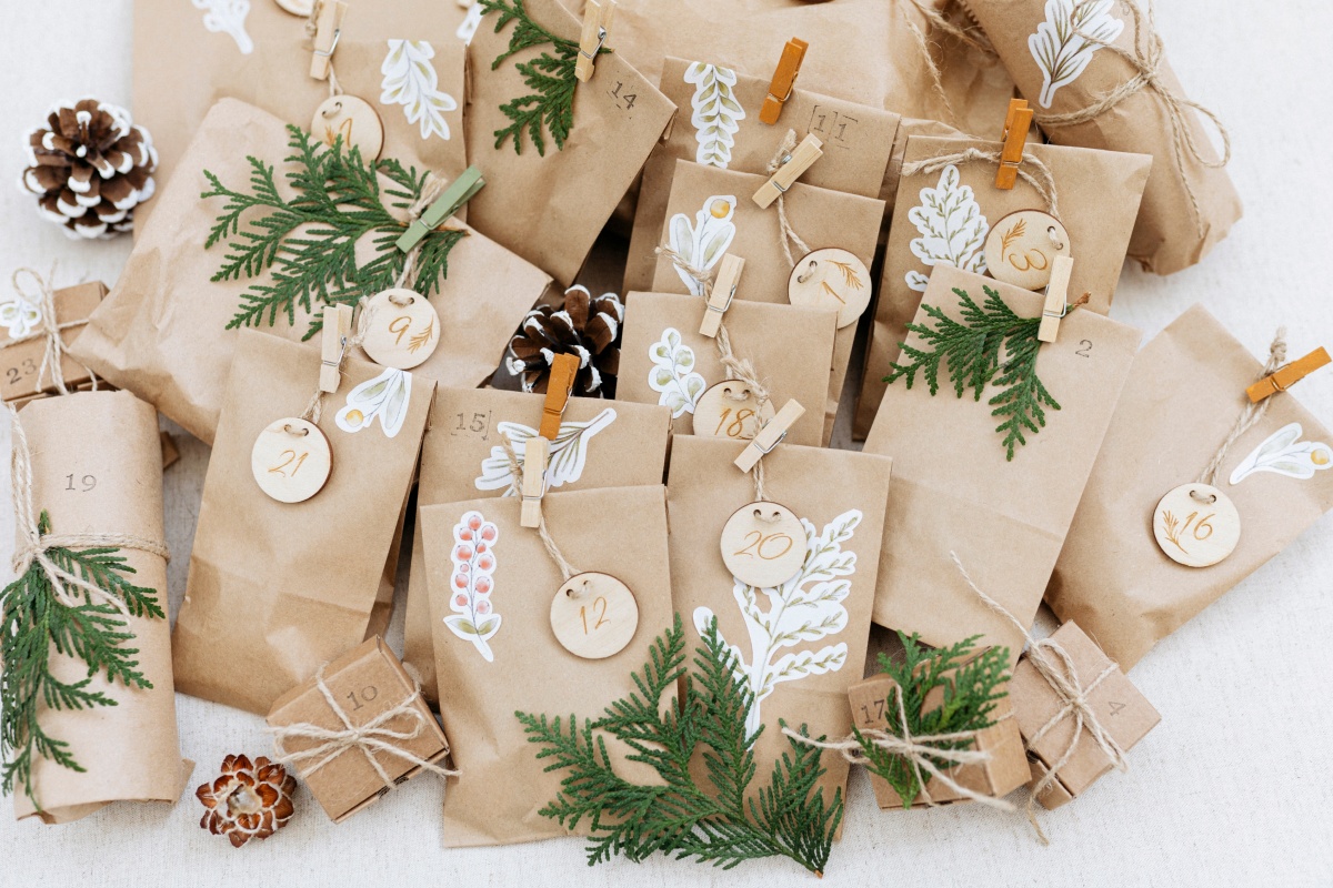 Adventskalender aus hellbraunen Papiertüten mit Holzanhängern und grünen Zweigen.