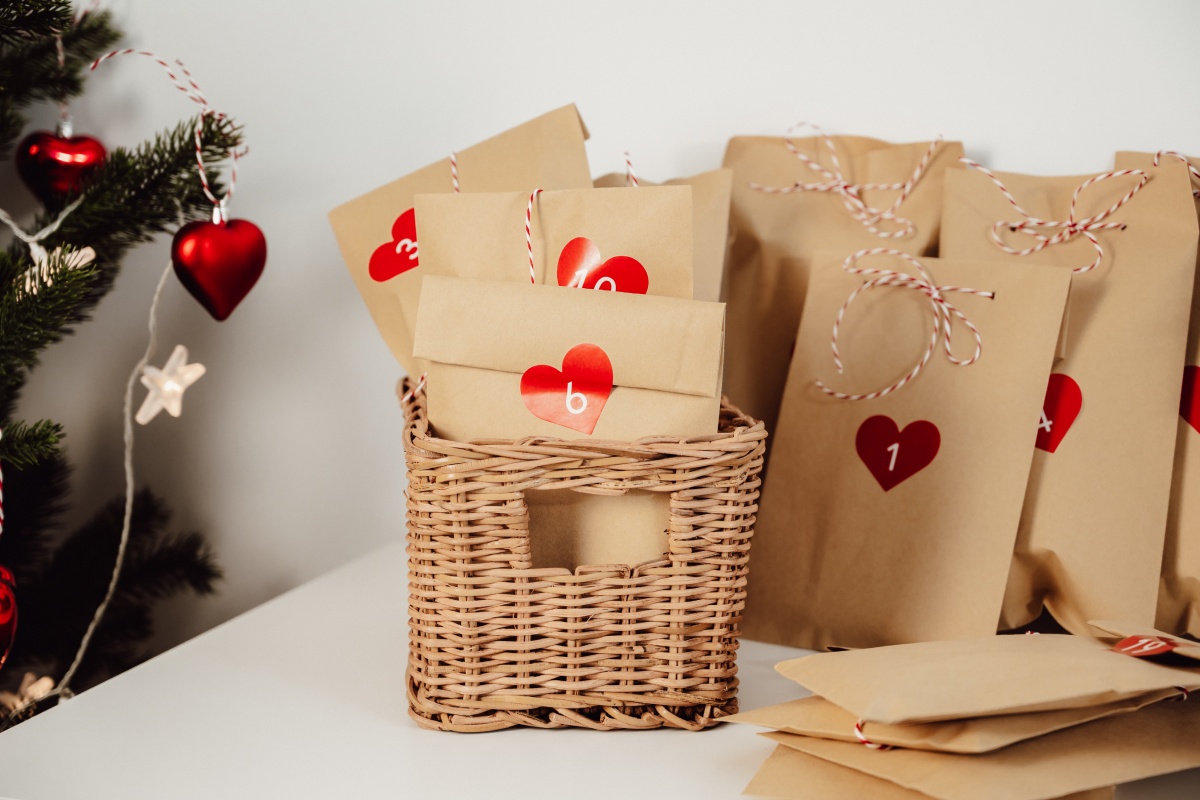 Adventskalender aus befüllte Papiertüten mit Herzverzierung stehen in einem Bastkorb.