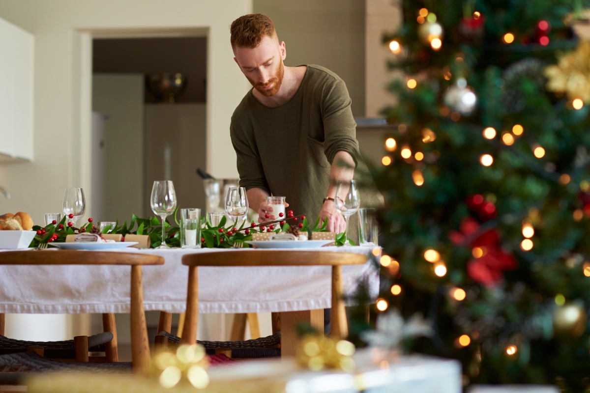 Mann dekoriert festlich gedeckten Tisch für Weihnachtsessen..