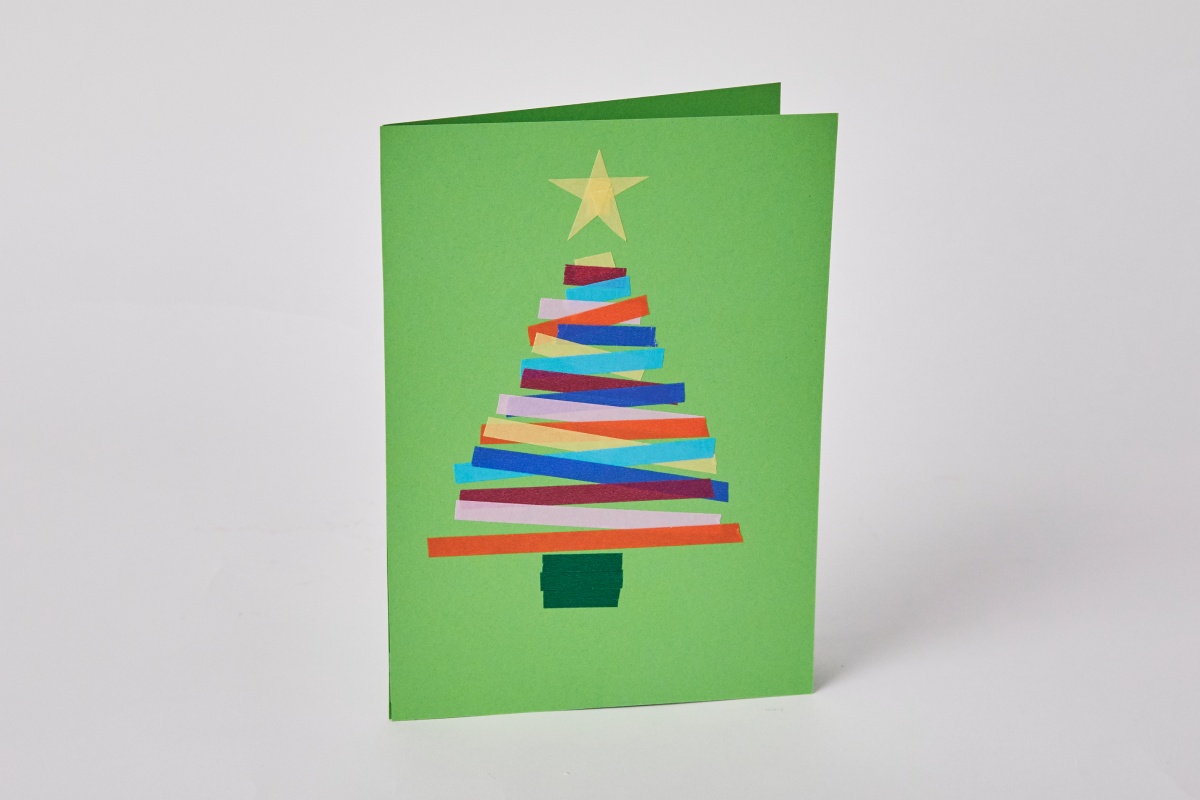 Selbstgebastelte Weihnachtskarte mit buntem Papierstreifen-Tannenbaum und gelbem Stern auf grünem Hintergrund.