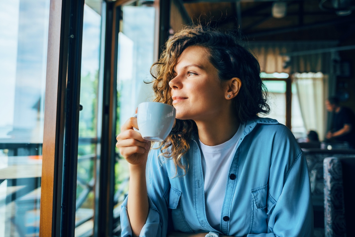 Frau mit Teetasse in der Hand schaut zufrieden aus dem Fenster