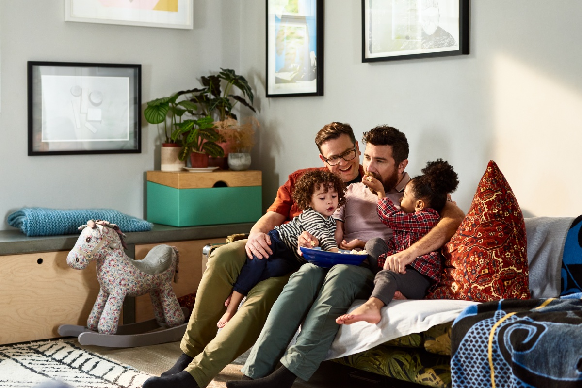 Zwei Männer sitzen mit ihren Kindern gemütlich auf dem Sofa im Wohnzimmer