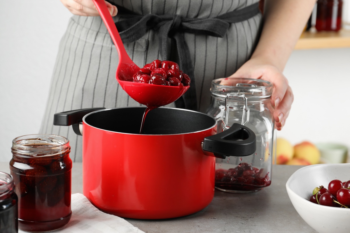 Person füllt Kirschkompott mit einer Kelle in ein Glas zur Vorbereitung für das Einkochen im Backofen.