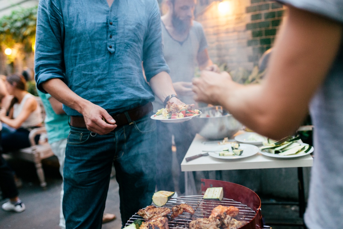 Partygäste holen sich mariniertes Fleisch und Gemüse vom Grill.