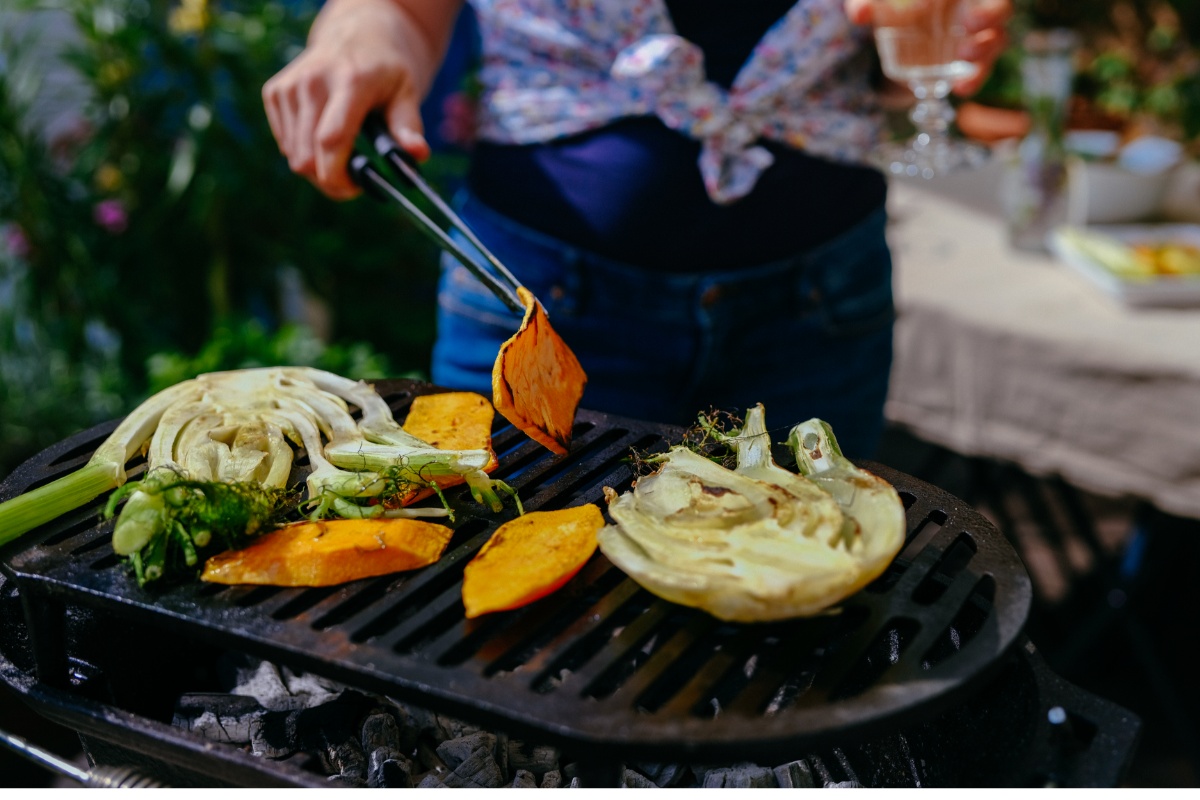 Person grillt Gemüse wie Kürbis und Fenchel auf einem Grill.