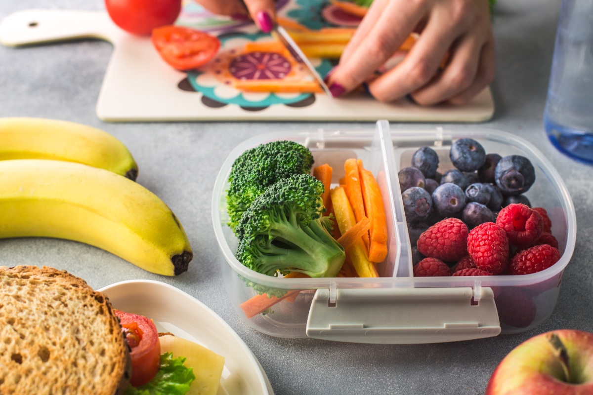 Jemand bereitet eine Brotdose aus Obst und Gemüse vor.