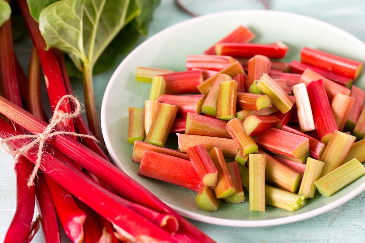 Zum Einfrieren vorbereiteter Rhabarber in Stücke geschnitten, daneben frische Rhabarberstangen.