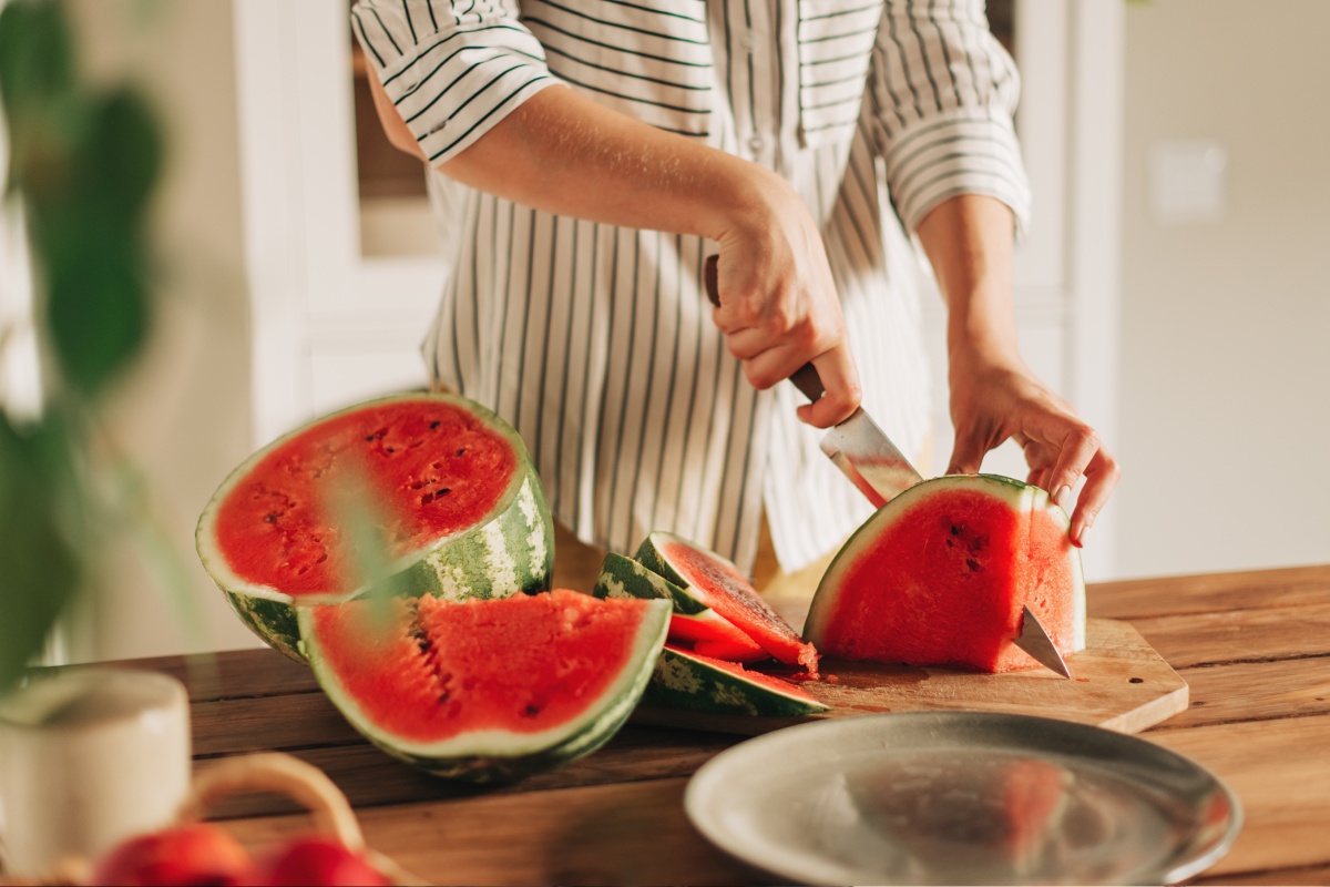 Eine Person schneidet eine reife Wassermelone auf einem Küchenbrett in Scheiben
