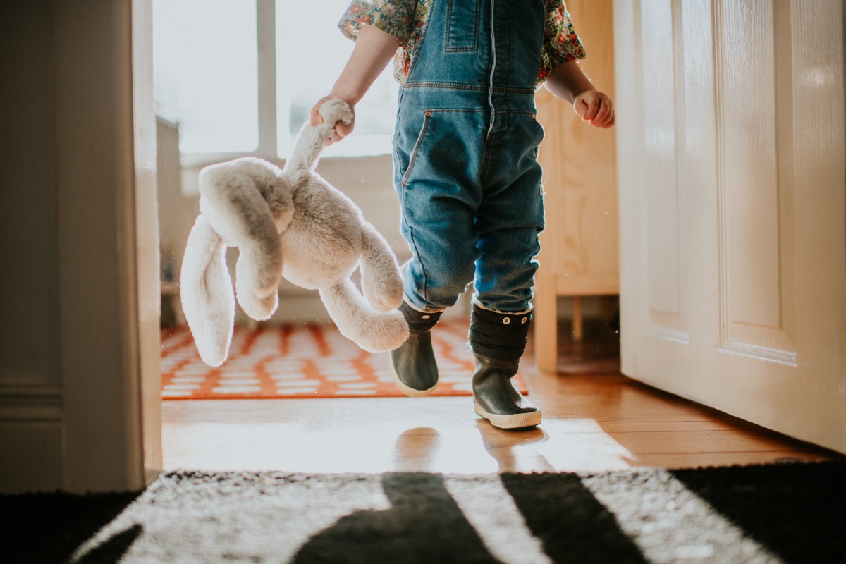 Eine Kleinkind läuft mit seinem Kuscheltier durch das Haus.