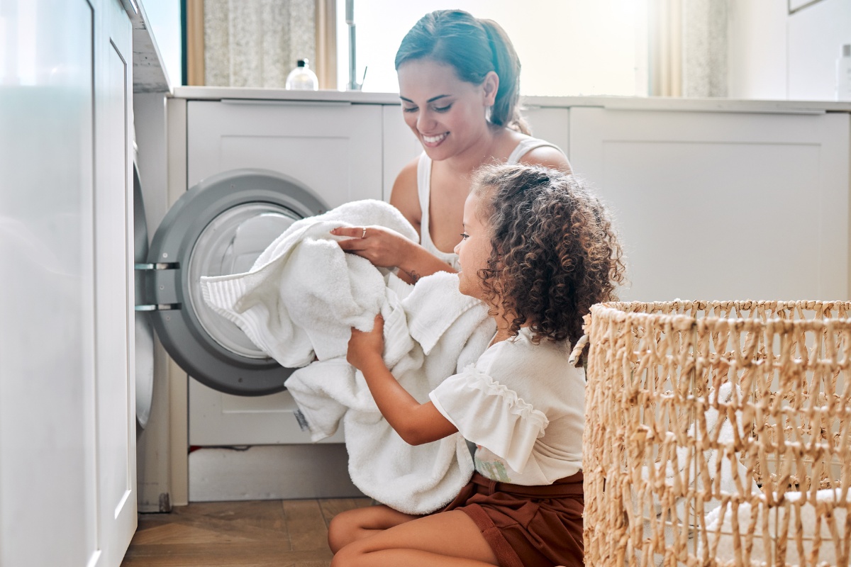 Eine Frau und ein Mädchen räumen gemeinsam weiße Wäsche in die Waschmaschine.