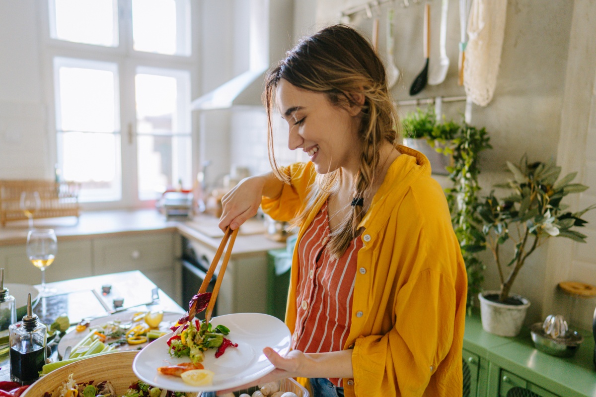 Eine junge Frau nimmt sich Salat auf den Teller.