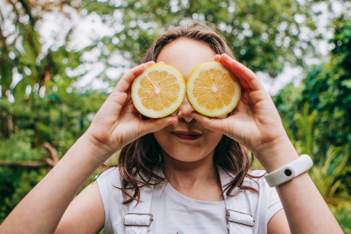 Ein junges Mädchen hält sich zwei Zitronenhälften als Brille vor die Augen