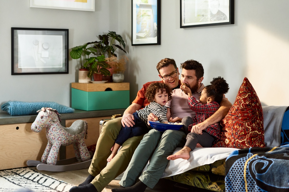 Zwei Männer sitzen mit ihren Kindern gemütlich auf dem Sofa im Wohnzimmer
