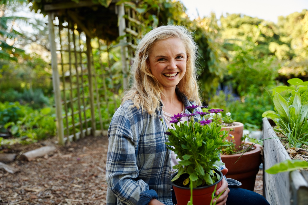 Eine Frau in einem grünen Garten mit einer blühenden Topfpflanze in der Hand