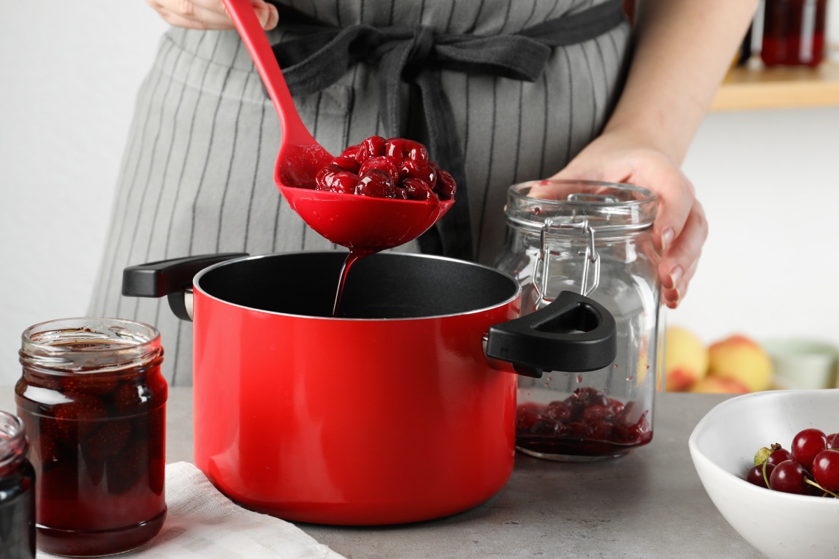 Person füllt Kirschkompott mit einer Kelle in ein Glas zur Vorbereitung für das Einkochen im Backofen.