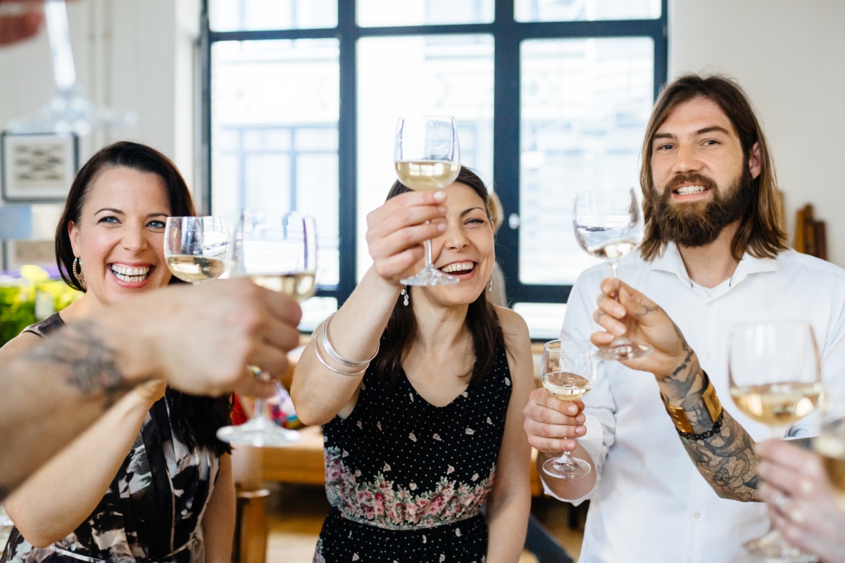 Gruppe von Freunden stößt mit Weißweingläsern an, alle lächeln und sind fröhlich.