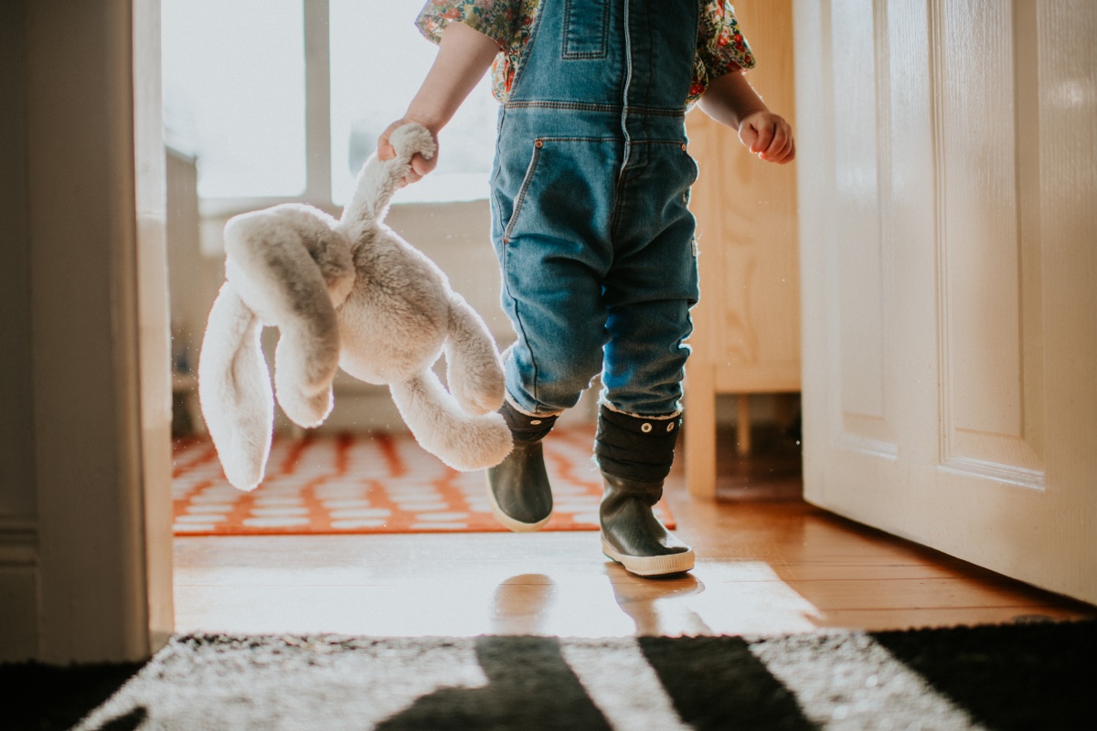Eine Kleinkind läuft mit seinem Kuscheltier durch das Haus.