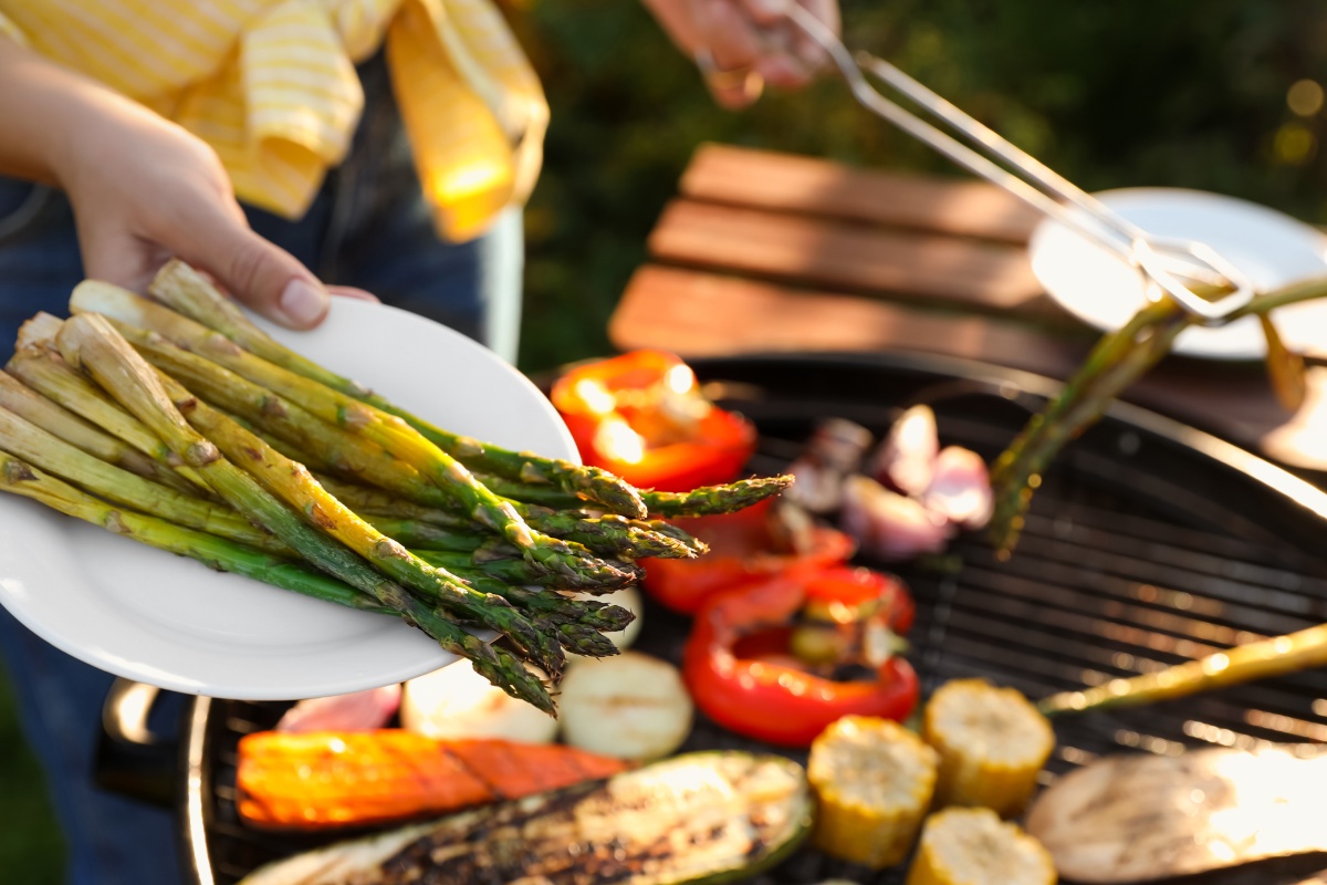 Gegrillter grüner Spargel auf einem Teller. Im Hintergrund verschiedenes gegrilltes Gemüse auf dem Grill.