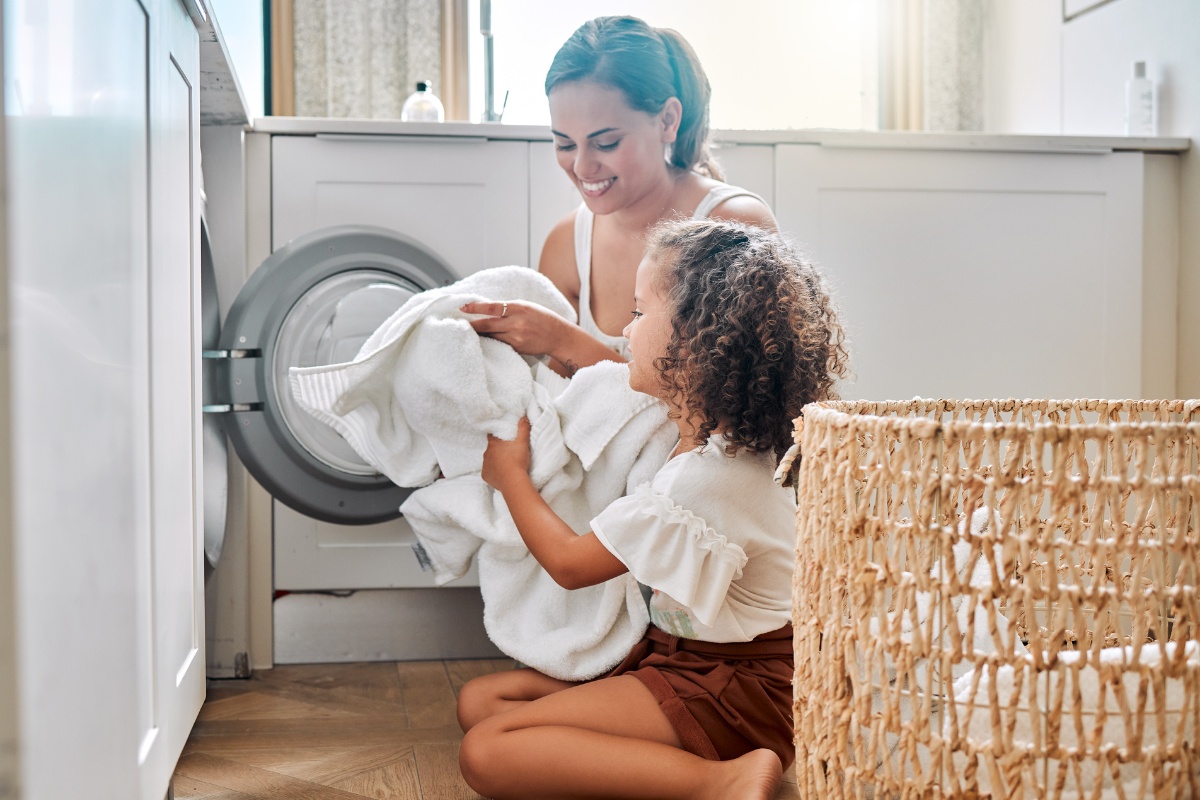 Eine Frau und ein Mädchen räumen gemeinsam weiße Wäsche in die Waschmaschine.