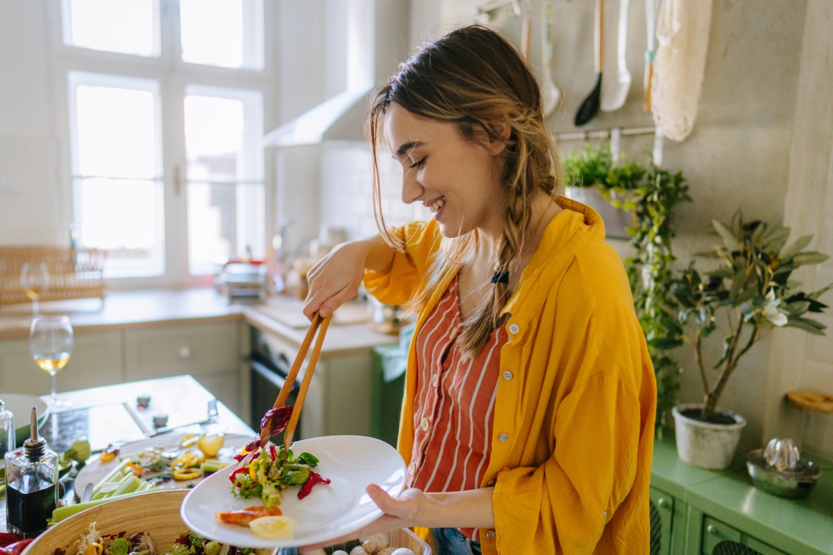 Eine junge Frau nimmt sich Salat auf den Teller.