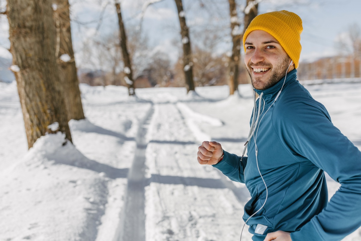 Ein Mann mit Sportkleidung und Mütze joggt auf schneebedeckter Laufstrecke im Winter.