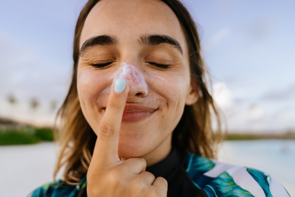 Eine junge Frau cremt sich lächelnd die Nase mit Sonnencreme ein.
