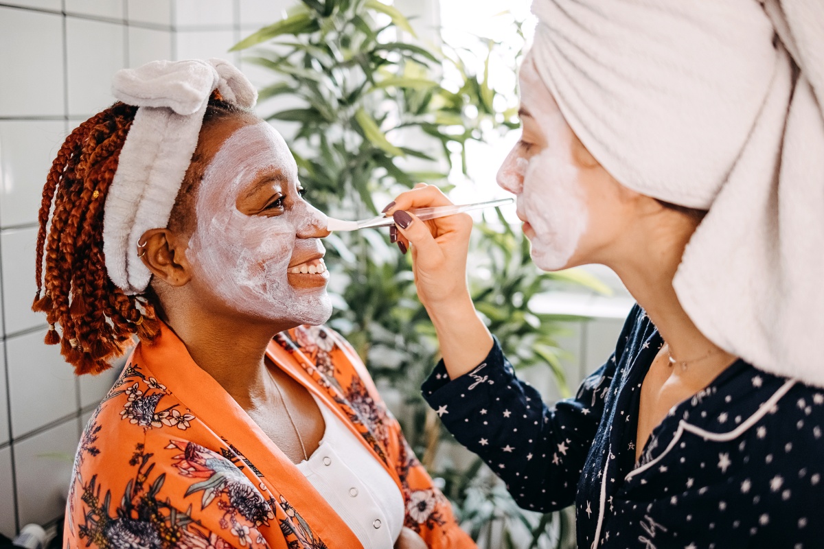 Zwei Freundinnen bepinseln ihre Gesichter mit einer Gesichtsmaske.
