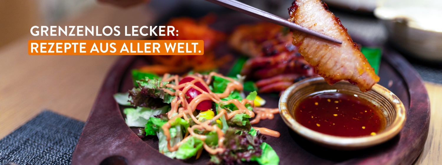 Gegrilltes Fleischstück in Stäbchen über einer Schale mit Soße, daneben frischer Salat mit Dressing, Nahaufnahme.