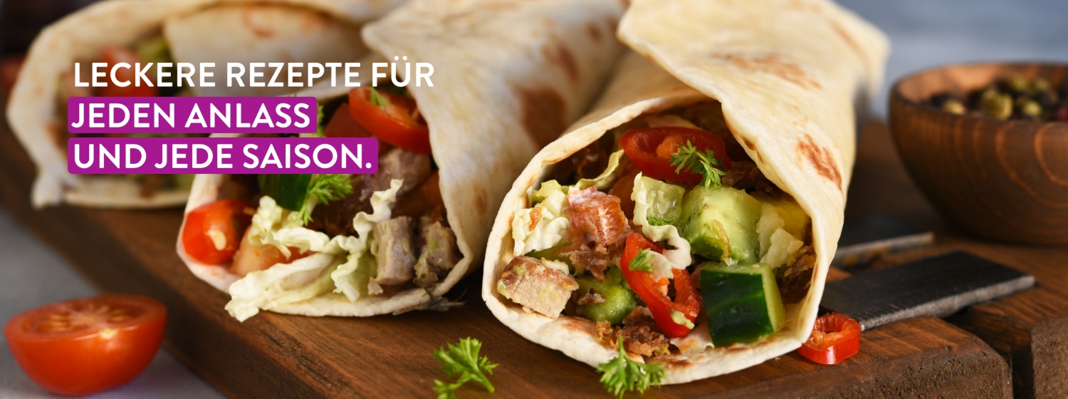 Drei gefüllte Wraps mit frischem Gemüse, Salat, Tomaten und Fleisch auf einem Holzbrett, nah aufgenommen.