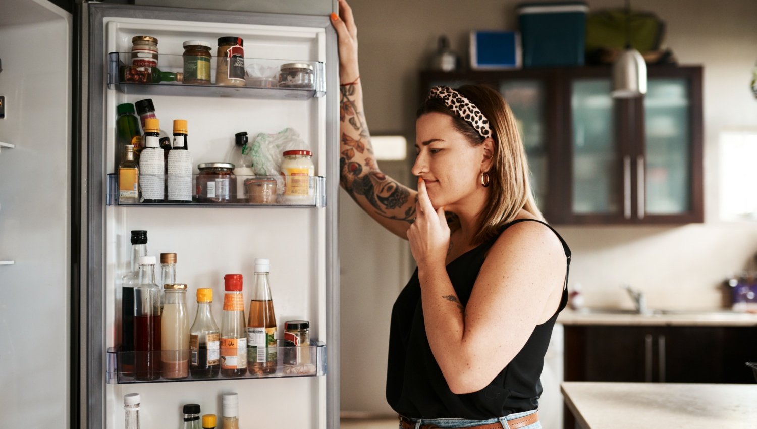 Eine Frau schaut in den offenen Kühlschrank, der mit verschiedenen Lebensmitteln gefüllt ist.
