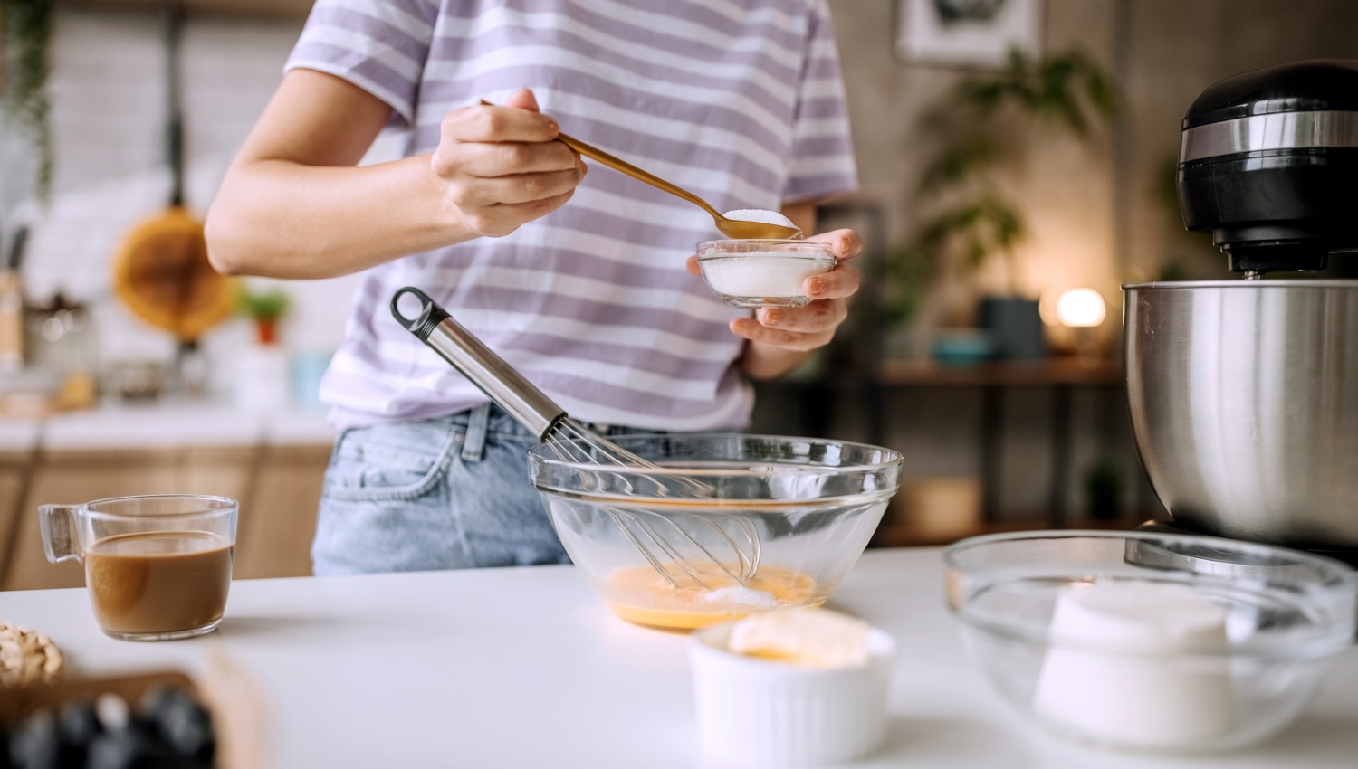 Person fügt Zucker in eine Schüssel mit Eiern, um einen Kuchen zu backen.