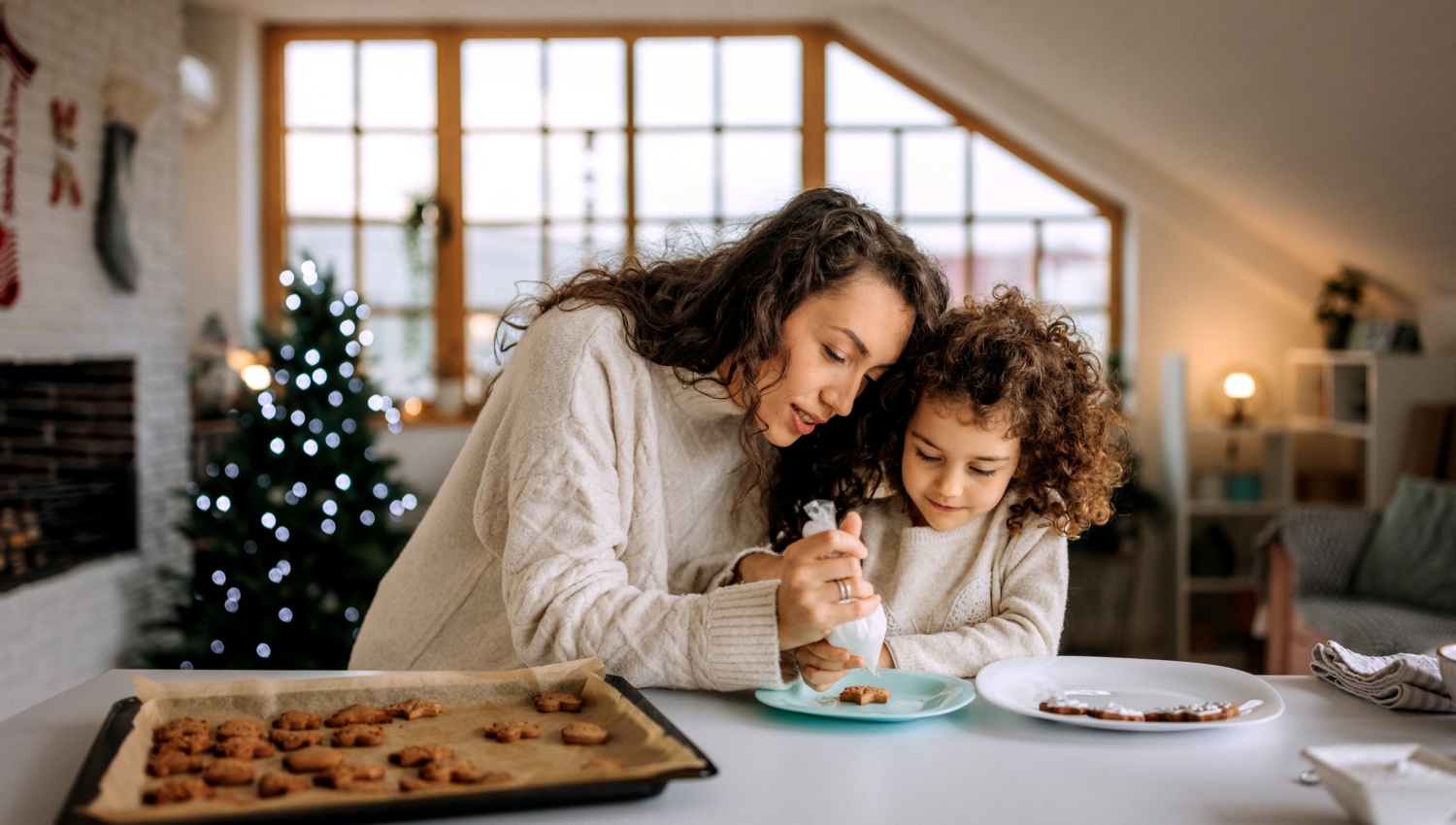 Mutter und Tochter verzieren frisch gebackene Plätzchen in einer weihnachtlich dekorierten Küche.