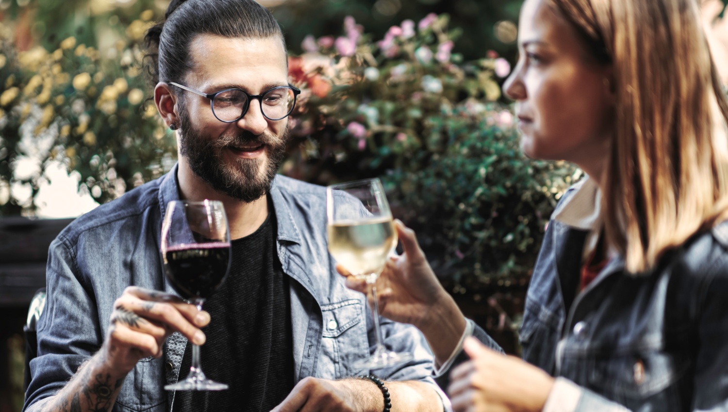 Zwei Personen stoßen mit Rot- und Weißwein im Freien an.