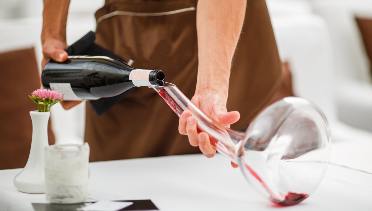 Ein Kellner dekantiert Rotwein in eine große Glaskaraffe, um den Wein zu belüften.