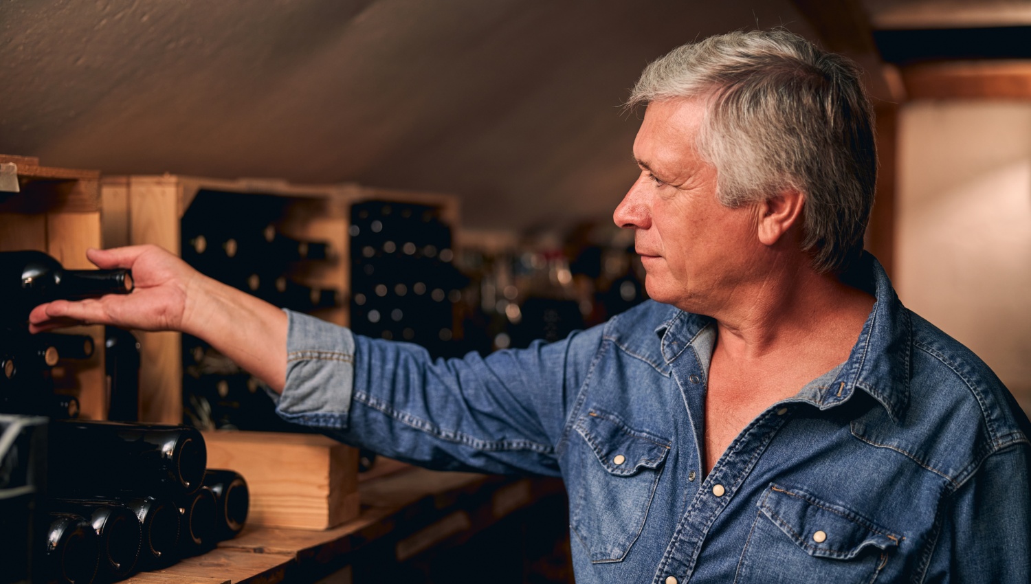 Mann legt eine Weinflasche zum Lagern in ein Weinregal.