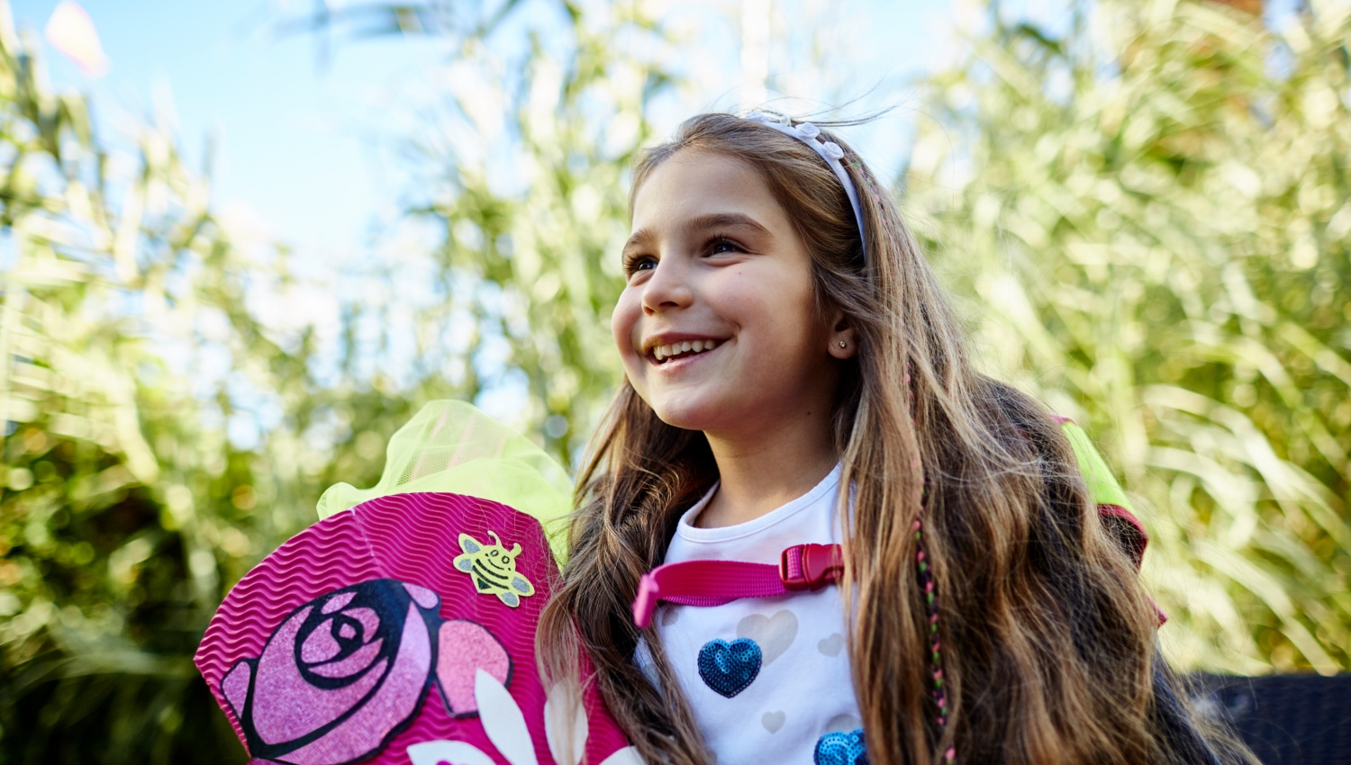 Fröhliches Mädchen mit rosa Schultüte und Schulrucksack im Freien.