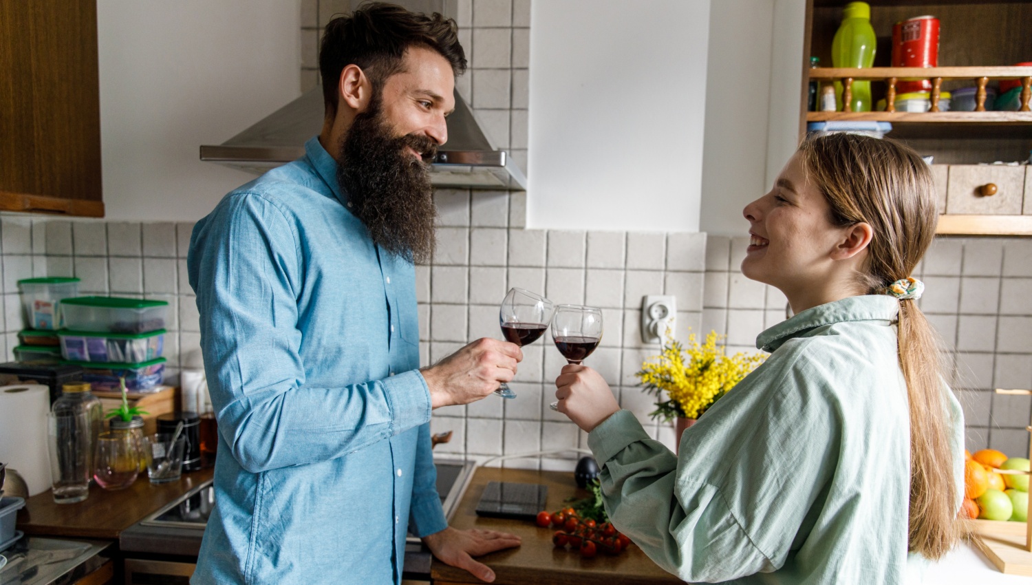 Mann und Frau in einer Küche schauen sich lächelnd in die Augen und stoßen mit Rotweingläsern an.